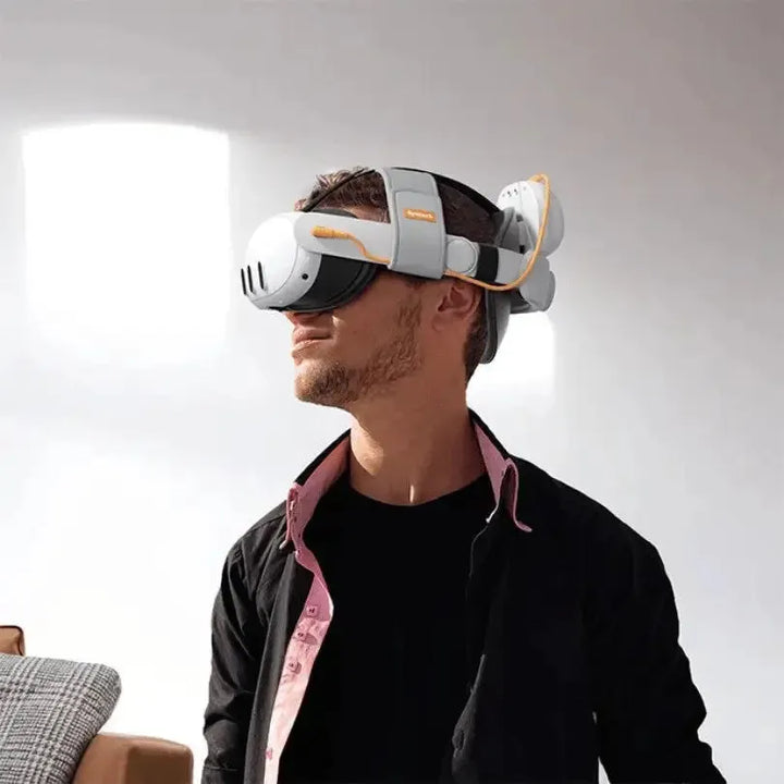 A person (likely male) from the chest up, wearing a white and grey VR headset with an orange and white comfort vr head strap that includes a battery pack on the back. The person is looking slightly to the right, and the background is a bright, minimalist interior.